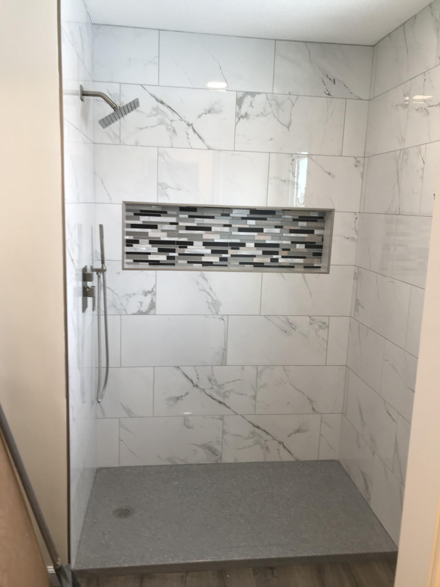 Finished walk-in shower with large marble-look tile and a mosaic storage niche