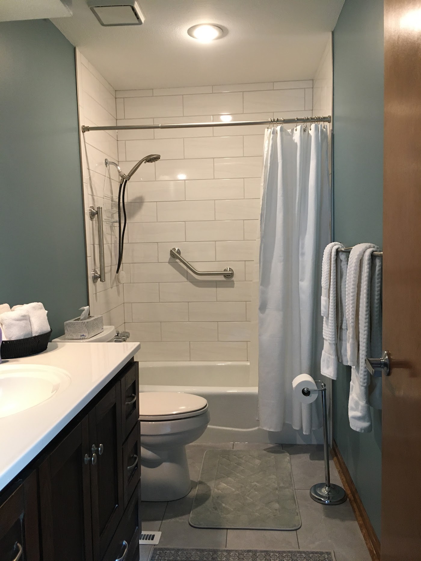 The same bathroom after remodel with white subway tile, soft blue-green walls, and a new tub surround